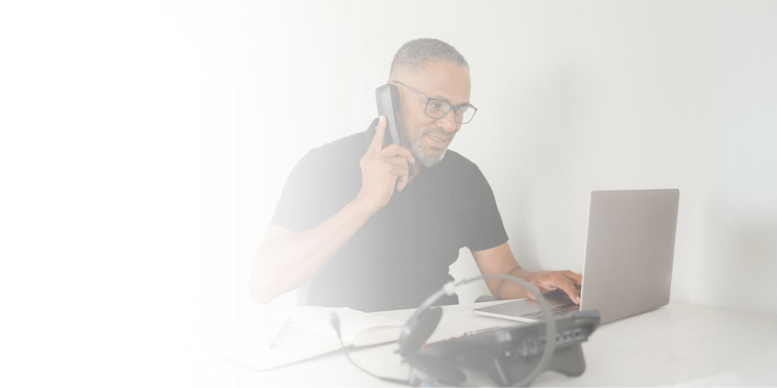 Profesional de TI en su escritorio, hablando por teléfono mientras trabaja en una laptop, simbolizando la contratación de talento remoto.