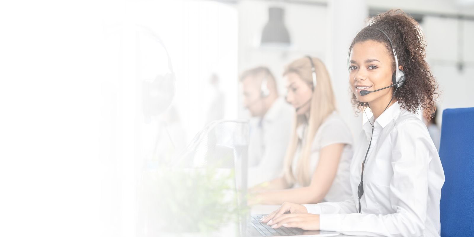 Centro de atención telefónica con operadores bilingües, destacando a una mujer sonriente con diadema, tecleando en su computadora.
